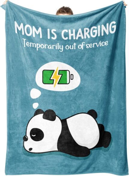 A blue-green Craftique throw blanket with "Mom is Charging" text, folded on a sofa, representing a cozy gift for moms.