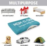 A blue-green Craftique throw blanket with "Mom is Charging" text, folded on a sofa, representing a cozy gift for moms.