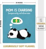 A blue-green Craftique throw blanket with "Mom is Charging" text, folded on a sofa, representing a cozy gift for moms.
