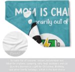 A blue-green Craftique throw blanket with "Mom is Charging" text, folded on a sofa, representing a cozy gift for moms.