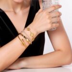 Close-up of four GIVCHO 18K gold plated stainless steel bangle bracelets with clear cubic zirconia stones.