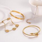 Close-up of four GIVCHO 18K gold plated stainless steel bangle bracelets with clear cubic zirconia stones.
