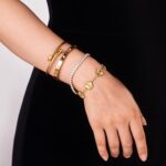 Close-up of four GIVCHO 18K gold plated stainless steel bangle bracelets with clear cubic zirconia stones.