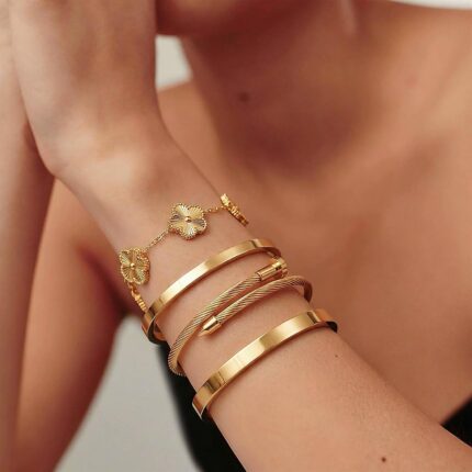 Two ISELBDR 18K gold plated stainless steel bangles, one with a clover design and one with a nail design, stacked together.