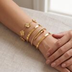 Two ISELBDR 18K gold plated stainless steel bangles, one with a clover design and one with a nail design, stacked together.