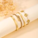 Two ISELBDR 18K gold plated stainless steel bangles, one with a clover design and one with a nail design, stacked together.