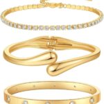 Four gold-plated bracelets, including a floral clover, tennis, chunky twist cuff, and classic bangle, stacked on a wrist.