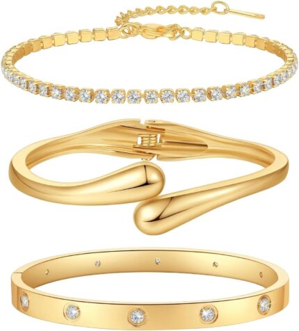 Four gold-plated bracelets, including a floral clover, tennis, chunky twist cuff, and classic bangle, stacked on a wrist.