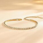 Four gold-plated bracelets, including a floral clover, tennis, chunky twist cuff, and classic bangle, stacked on a wrist.