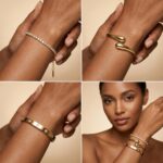 Four gold-plated bracelets, including a floral clover, tennis, chunky twist cuff, and classic bangle, stacked on a wrist.