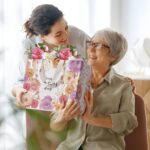 Two large pink floral gift bags with handles, tissue paper, greeting cards, and stickers for Mother's Day gifts.